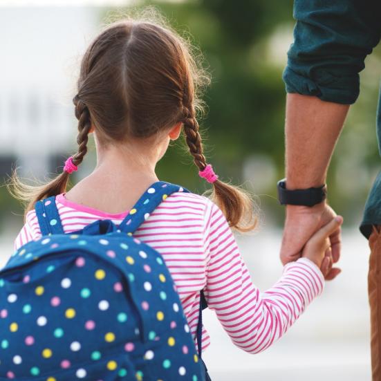 Pige går med skoletaske og sin far i hånden