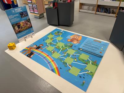 Foto af spillepladen på gulvet, en infotavle og en gul skumterning.